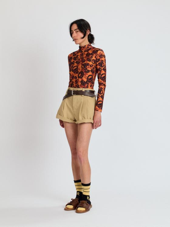 A woman wearing an orange printed Meryll Rogge turtleneck with khaki pleated shorts and brown sandals