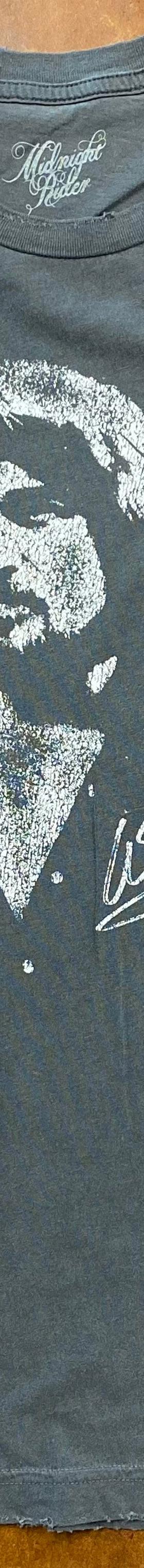 A faded blue Midnight Rider graphic t-shirt laid flat on a brown leather surface