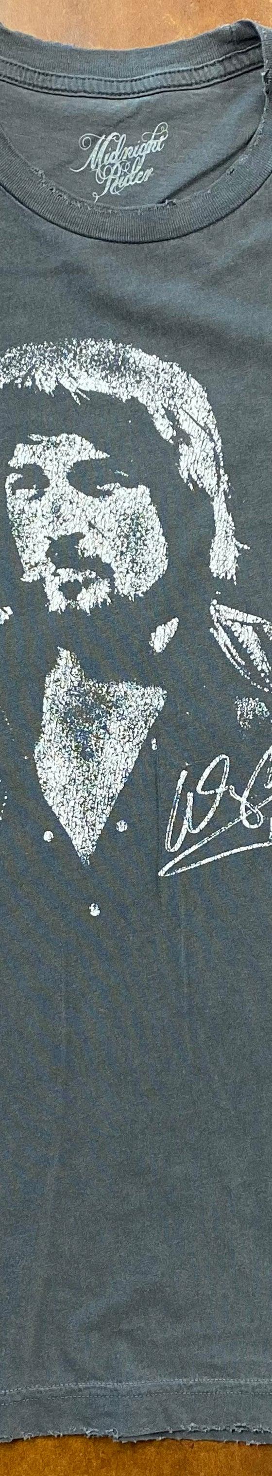A faded blue Midnight Rider graphic t-shirt laid flat on a brown leather surface