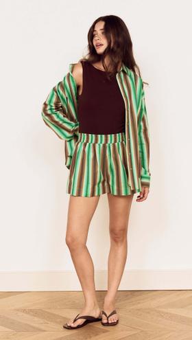 A woman wearing a green striped MinkPink shirt and matching shorts over a brown tank top