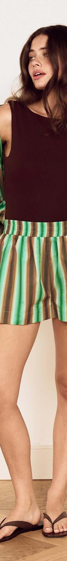 A woman wearing a green striped MinkPink shirt and matching shorts over a brown tank top