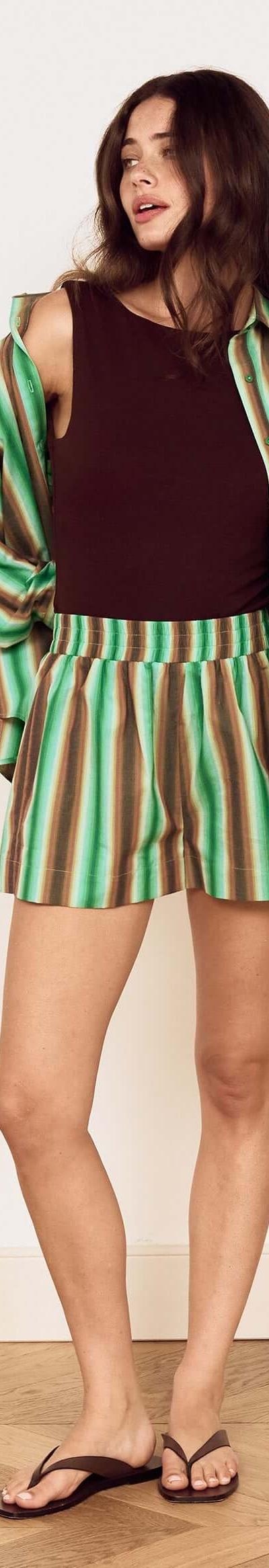 A woman wearing a green striped MinkPink shirt and matching shorts over a brown tank top
