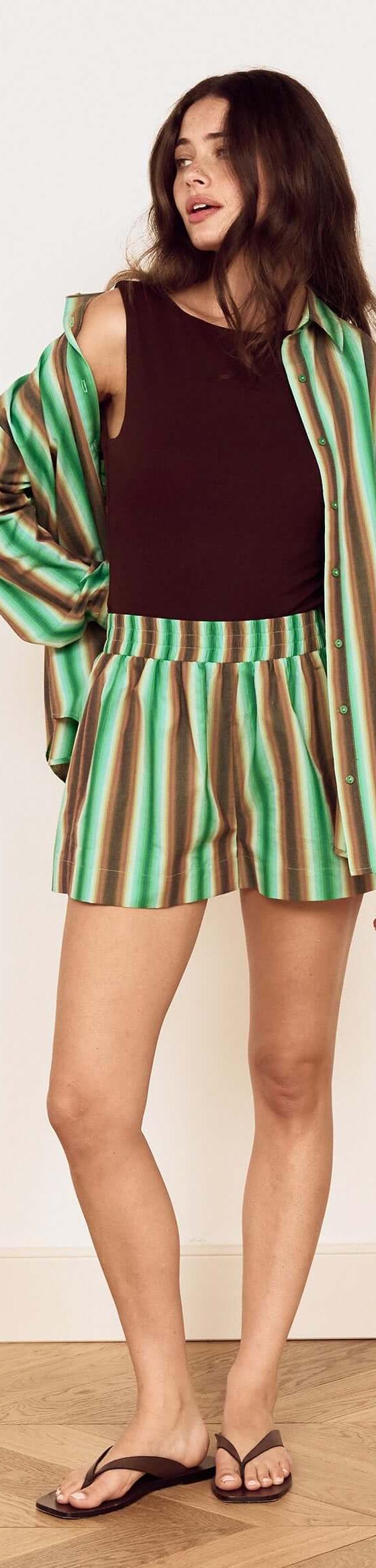 A woman wearing a green striped MinkPink shirt and matching shorts over a brown tank top