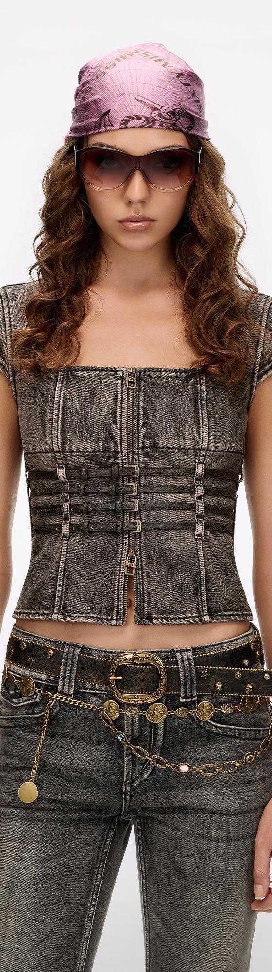 A woman wearing a Miss Sixty washed denim corset top with low-rise grey jeans, a chain belt and pink bandana cap