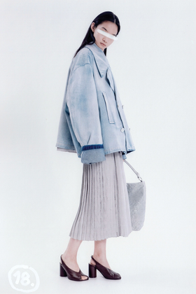 A woman wearing an oversized washed-denim MM6 Maison Margiela jacket with a pleated midi skirt and Tabi mules