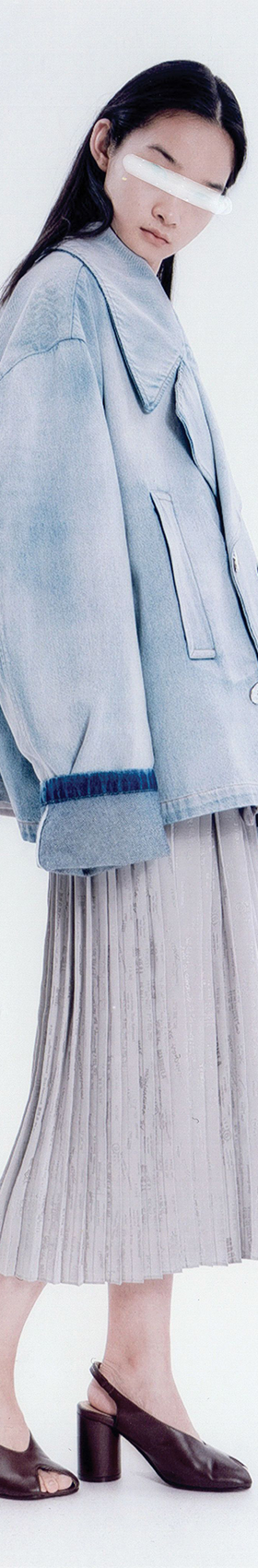 A woman wearing an oversized washed-denim MM6 Maison Margiela jacket with a pleated midi skirt and Tabi mules