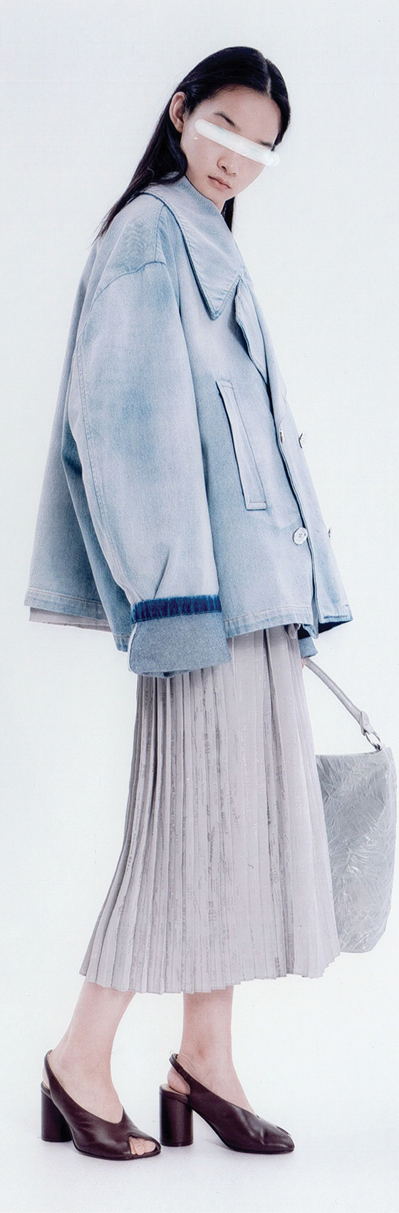 A woman wearing an oversized washed-denim MM6 Maison Margiela jacket with a pleated midi skirt and Tabi mules