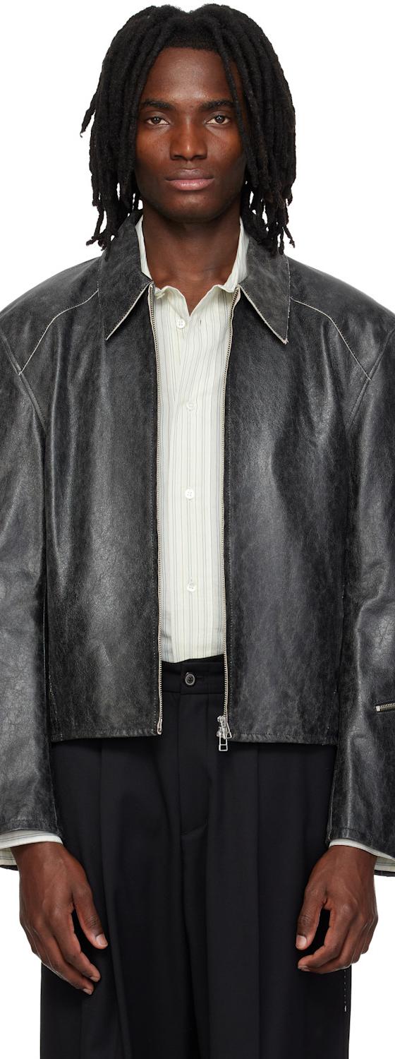 A man wearing a distressed grey leather jacket over a striped shirt and black wide-leg trousers