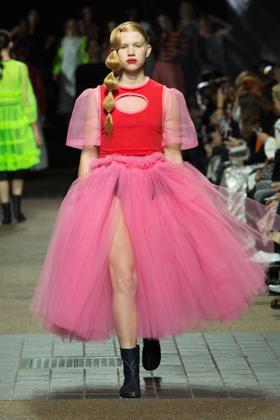 A model wearing a voluminous pink tulle Molly Goddard skirt with a red top on the runway