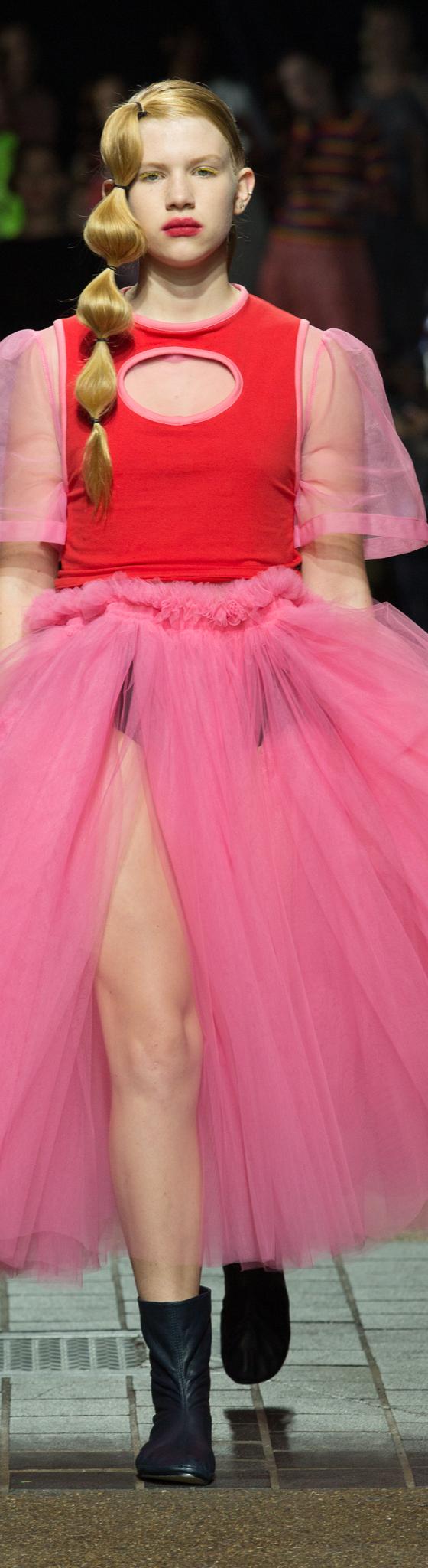 A model wearing a voluminous pink tulle Molly Goddard skirt with a red top on the runway