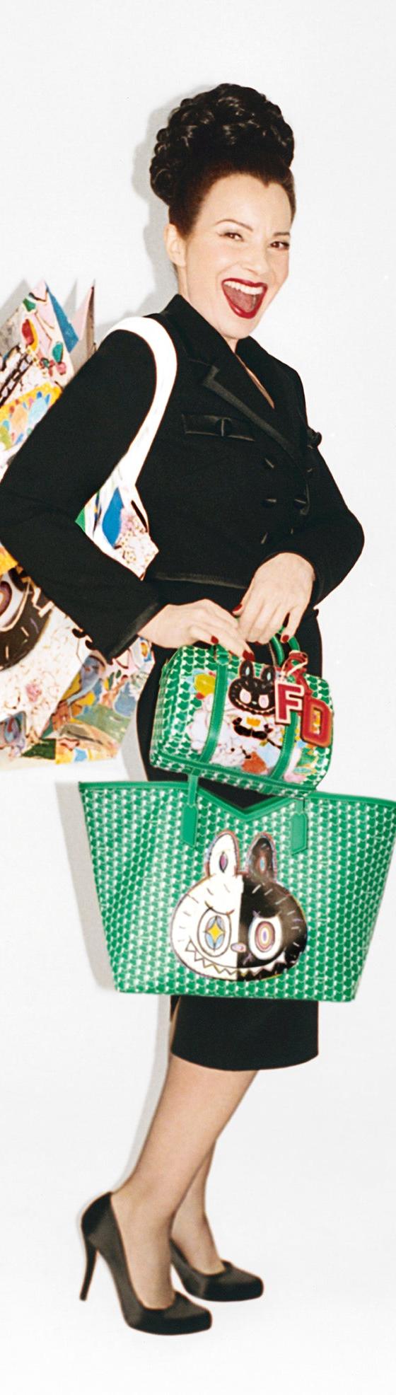 A woman in a black skirt suit and heels carrying green monogram-pattern Moynat tote and top-handle bags