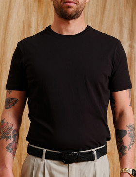 A man wearing a black Mr Simple t-shirt with beige pleated trousers