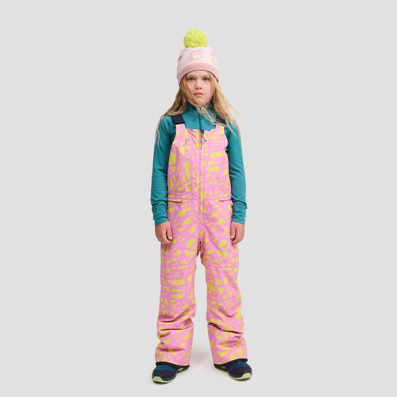 A girl wearing a pink and yellow printed namuk snow bib with a teal base layer and pink pom-pom beanie