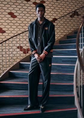 A man wearing a black Needles track jacket and matching wide-leg track pants over a polka dot shirt