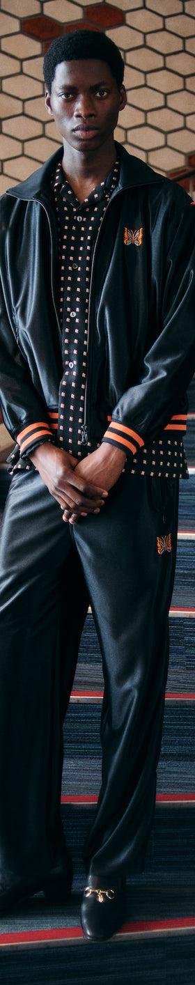A man wearing a black Needles track jacket and matching wide-leg track pants over a polka dot shirt