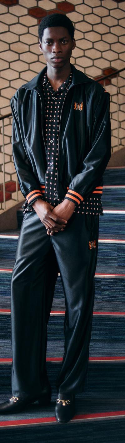 A man wearing a black Needles track jacket and matching wide-leg track pants over a polka dot shirt
