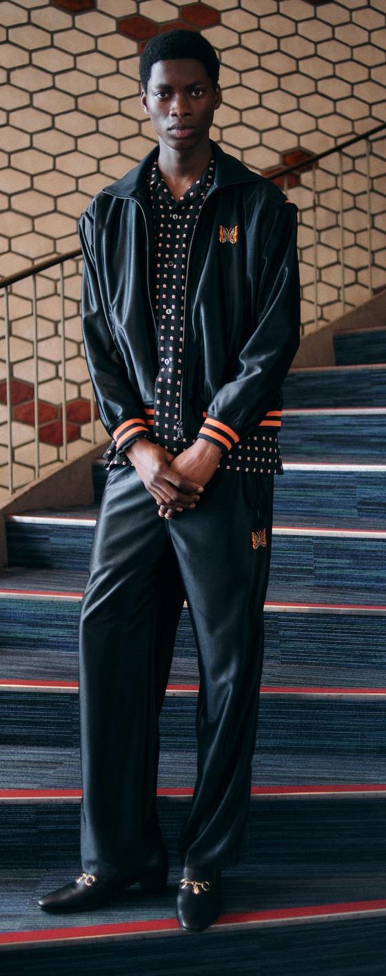 A man wearing a black Needles track jacket and matching wide-leg track pants over a polka dot shirt