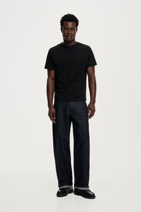 A man wearing a black Neuw T-shirt and dark straight-leg jeans