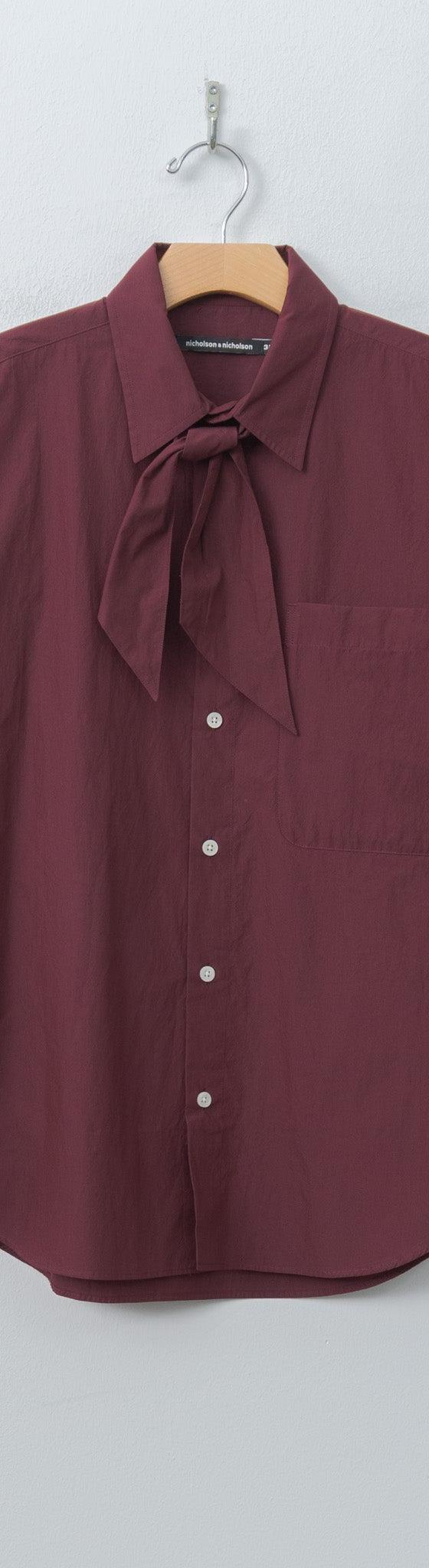 A burgundy Nicholson & Nicholson tie-neck cotton shirt on a hanger