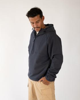 A man wearing a dark-ink NIKIN TreeHoodie quarter-zip fleece and tan trousers