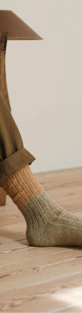 A person wearing olive ribbed NISHIGUCHI KUTSUSHITA socks with cuffed khaki trousers on a wooden floor