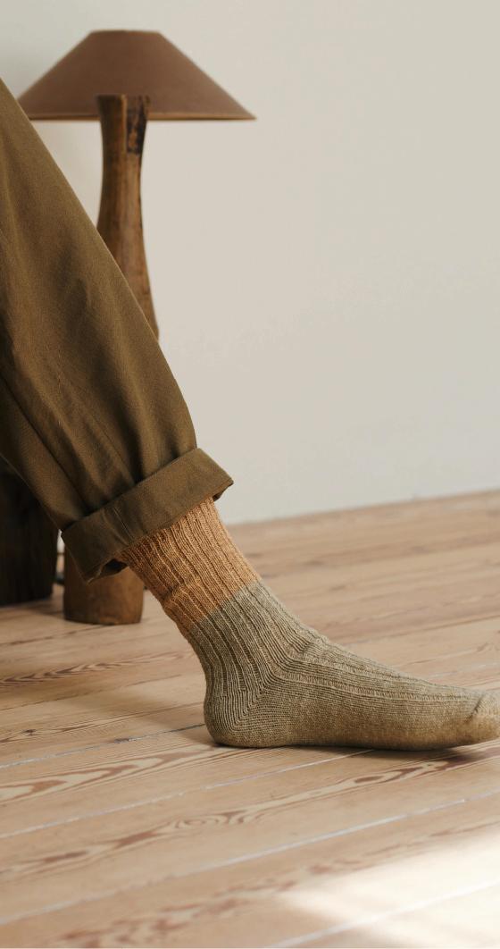 A person wearing olive ribbed NISHIGUCHI KUTSUSHITA socks with cuffed khaki trousers on a wooden floor