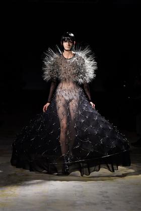 A woman wearing a sheer black Noir Kei Ninomiya gown with a spiked silver shoulder piece