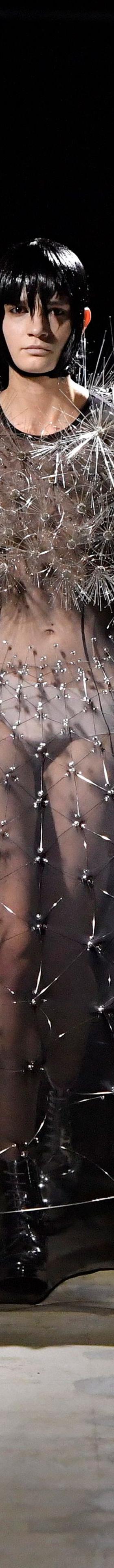 A woman wearing a sheer black Noir Kei Ninomiya gown with a spiked silver shoulder piece