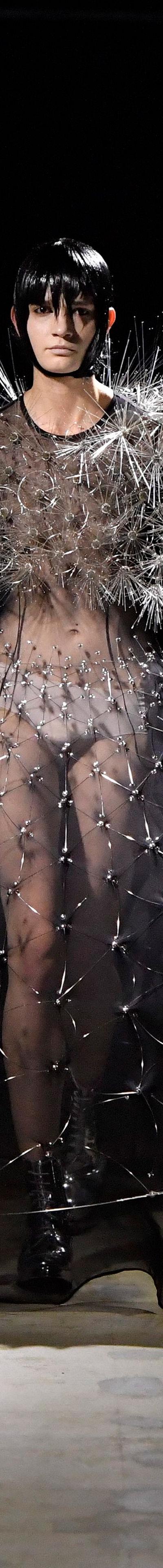 A woman wearing a sheer black Noir Kei Ninomiya gown with a spiked silver shoulder piece