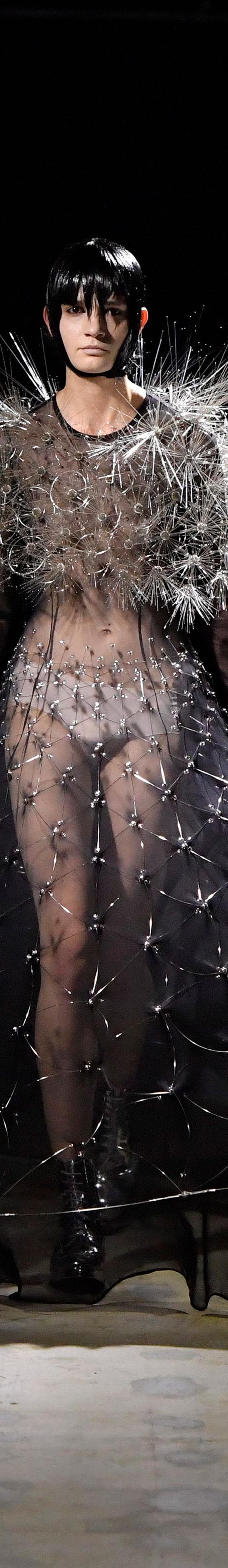 A woman wearing a sheer black Noir Kei Ninomiya gown with a spiked silver shoulder piece