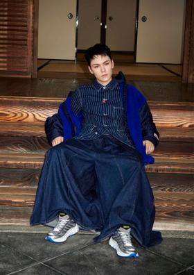 A model in an indigo denim workwear jacket and wide-leg jeans with grey and blue running sneakers