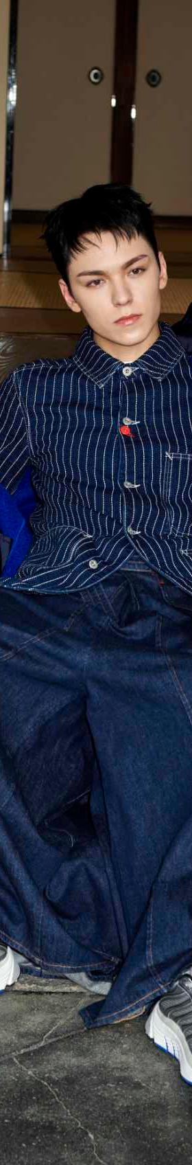 A model in an indigo denim workwear jacket and wide-leg jeans with grey and blue running sneakers