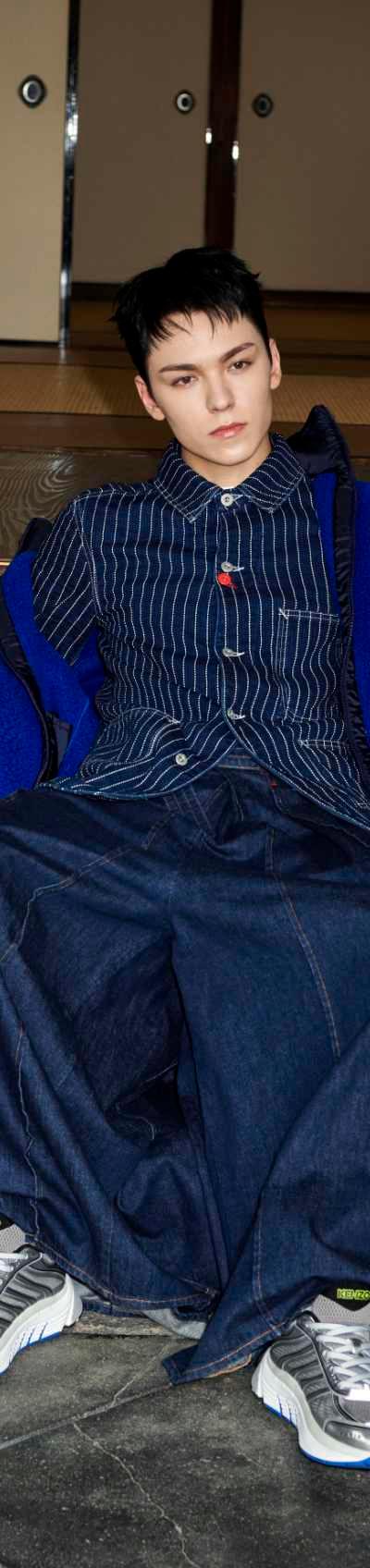 A model in an indigo denim workwear jacket and wide-leg jeans with grey and blue running sneakers