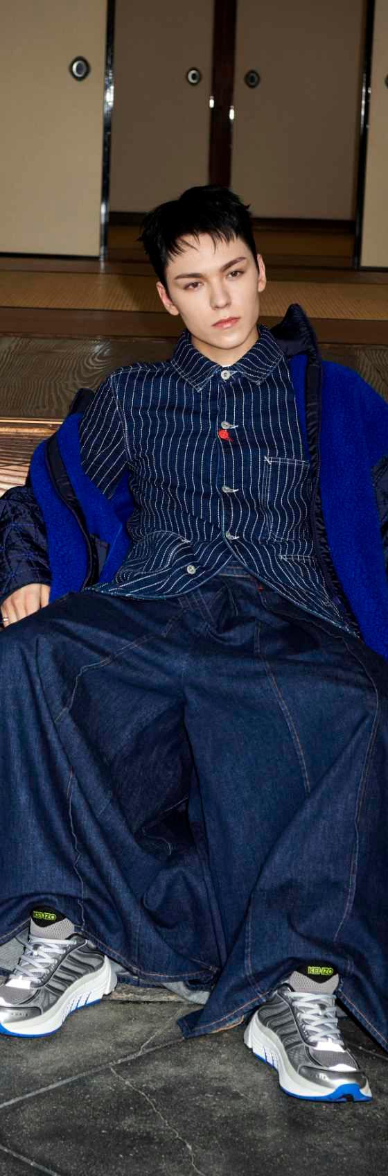 A model in an indigo denim workwear jacket and wide-leg jeans with grey and blue running sneakers