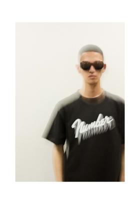 A man wearing sunglasses and a black NUMBER (N)INE script-logo T-shirt