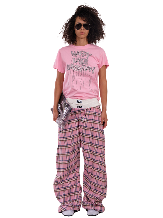 A woman wearing a pink NZKidzzz slogan T-shirt with pink checked wide-leg trousers