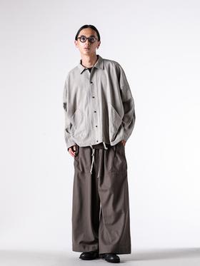 A man wearing a grey O-Project overshirt with wide brown trousers