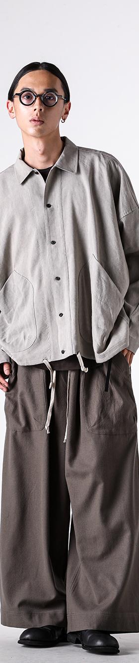 A man wearing a grey O-Project overshirt with wide brown trousers