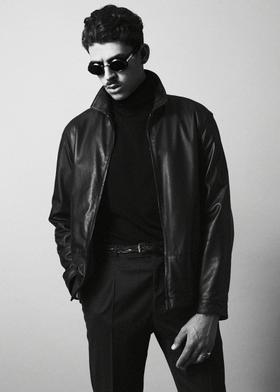 A man wearing a black O.Ballou leather jacket over a black turtleneck and tailored trousers