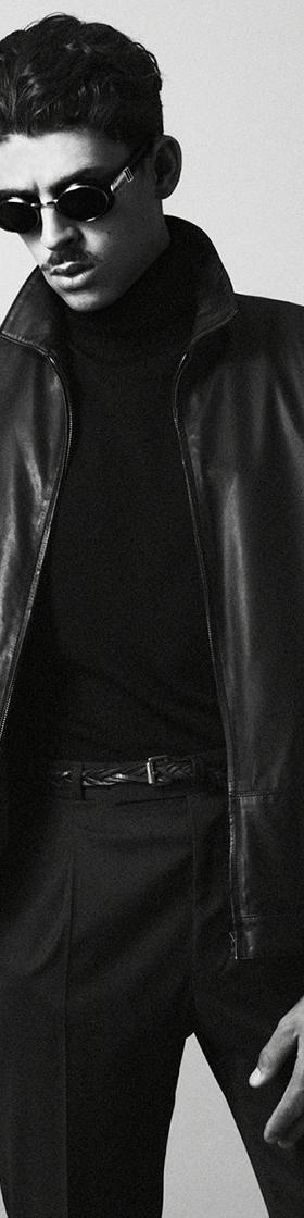 A man wearing a black O.Ballou leather jacket over a black turtleneck and tailored trousers