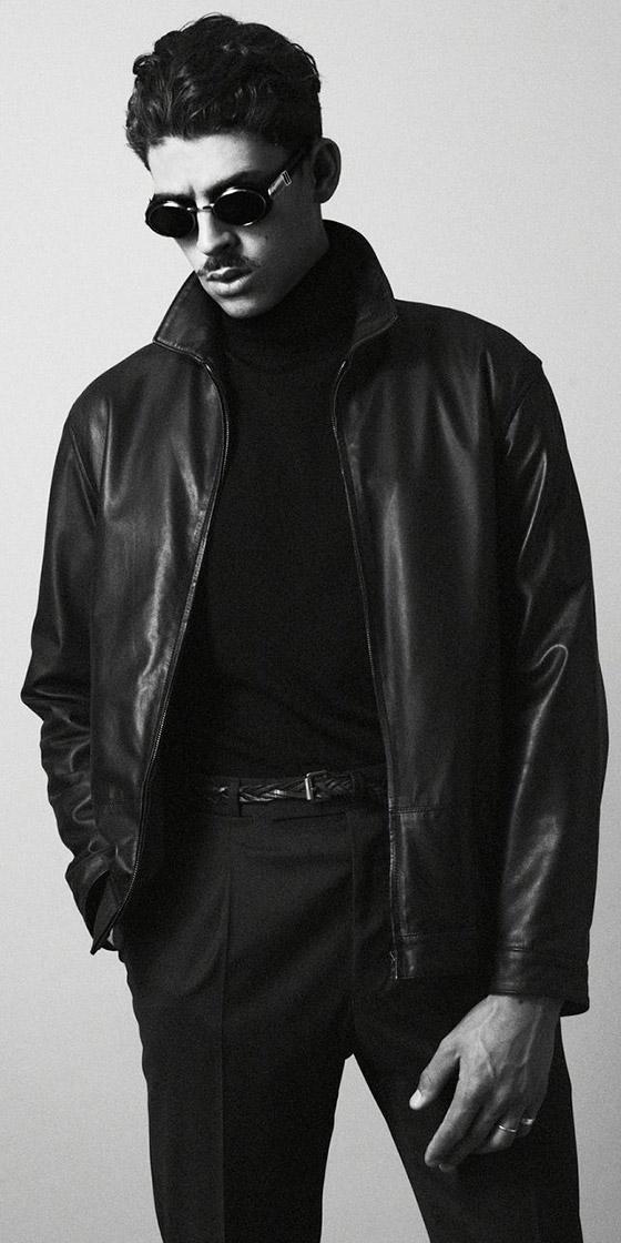 A man wearing a black O.Ballou leather jacket over a black turtleneck and tailored trousers