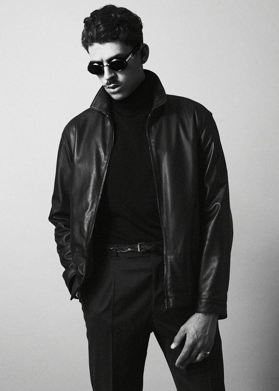A man wearing a black O.Ballou leather jacket over a black turtleneck and tailored trousers