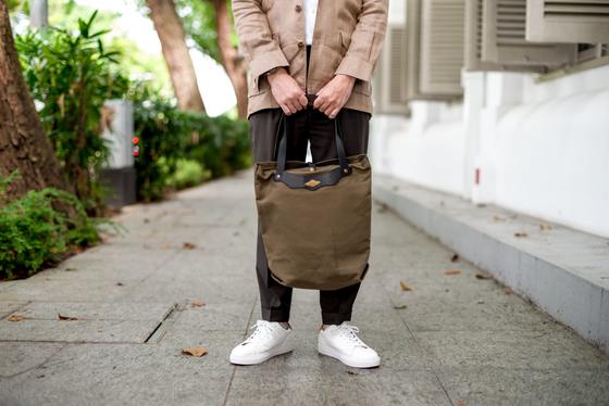 A man holding an olive canvas and leather tote bag from Obbi Good Label
