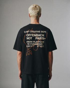 A man wearing a black OFFENBACH. NOT PARIS t-shirt with an orange and white back print