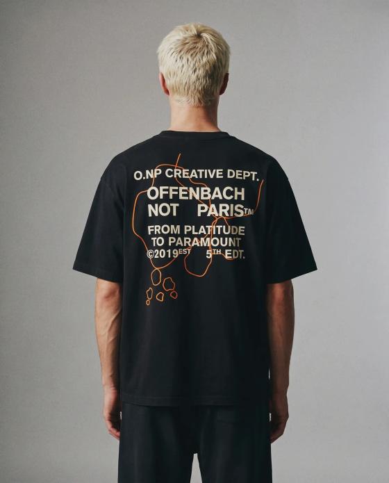 A man wearing a black OFFENBACH. NOT PARIS t-shirt with an orange and white back print