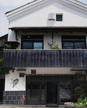 OKURA's kura-style storehouse shopfront in Daikanyama: white plaster gable, dark timber, plants, no people