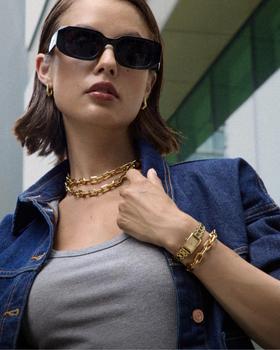 A woman wearing a gold Olivia Burton chain-link watch and necklace with a denim jacket