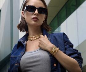 A woman wearing a gold Olivia Burton chain-link watch and necklace with a denim jacket