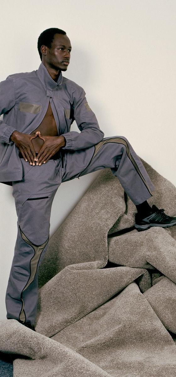 A man wearing a grey Olly Shinder technical jacket and matching curved-seam trousers