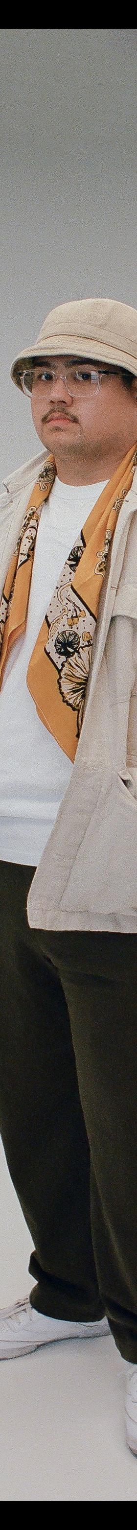 A man wearing a printed bandanna scarf with a cream overshirt and bucket hat